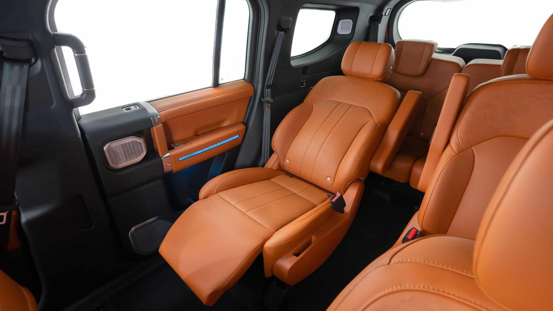 Interior do JETOUR G700 focado na segunda fileira de bancos, exibindo duas poltronas individuais em couro caramelo com descanso para as pernas, apoiado de braço e detalhes de iluminação ambiente azul
