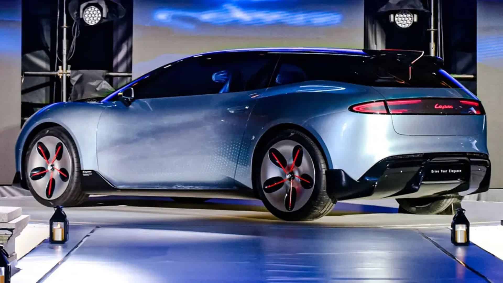 Visão lateral e frontal do LEPAS AURA Concept, destacando as linhas fluidas da carroceria azul metálico, o teto escuro e as rodas aerodinâmicas com detalhes vermelhos. A frente mostra os faróis 'Leopard-Eye' e a grade preta integrada com o logotipo 'Lepas'. Ao fundo, refletores de palco iluminam o veículo