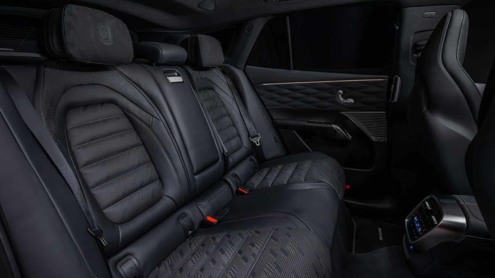 Vista do banco traseiro de um carro de luxo com estofamento em couro preto e tecido texturizado, apoios de cabeça macios, detalhes em costura e um console central traseiro com tela de controle de climatização