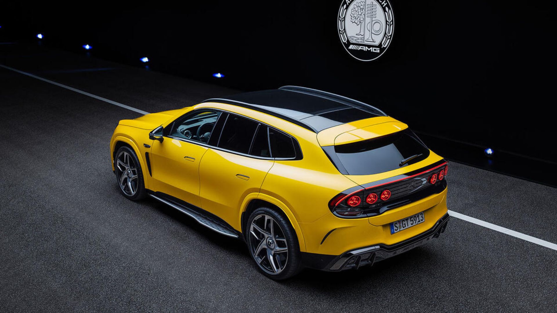 Vista traseira e lateral de um SUV esportivo amarelo brilhante estacionado em uma pista escura, destacando o teto panorâmico preto, rodas esportivas e a assinatura de seis luzes traseiras redondas com detalhes em vermelho
