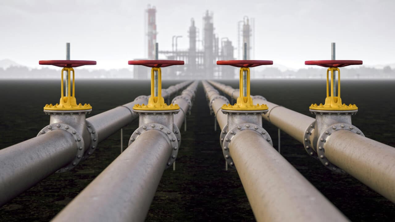 Imagem de oleodutos conduzindo a uma refinaria de petróleo ao fundo