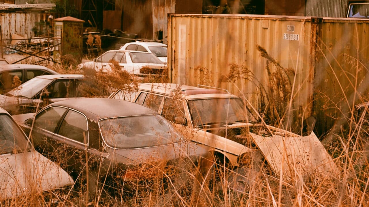 Carros abandonados num pátio, com capim crescendo