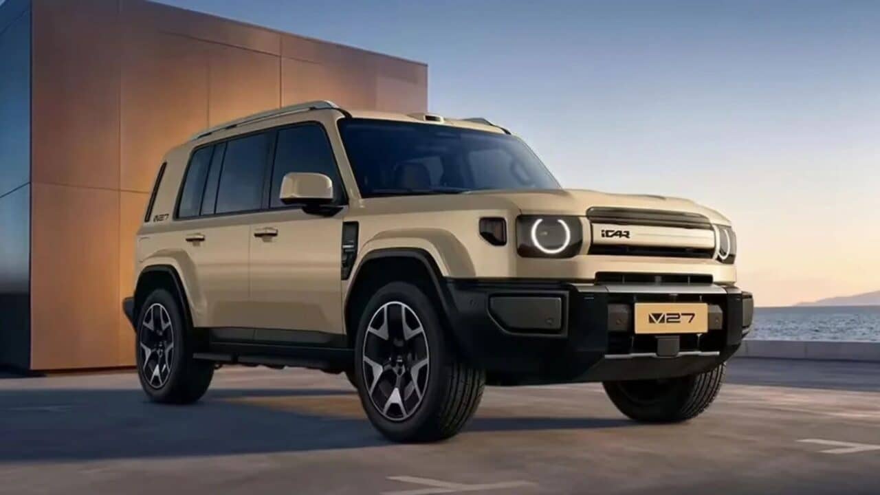 SUV iCar V27 bege visto de frente, estacionado em uma área externa ao lado de um prédio, com faróis redondos de LED e o logotipo iCAR na grade frontal