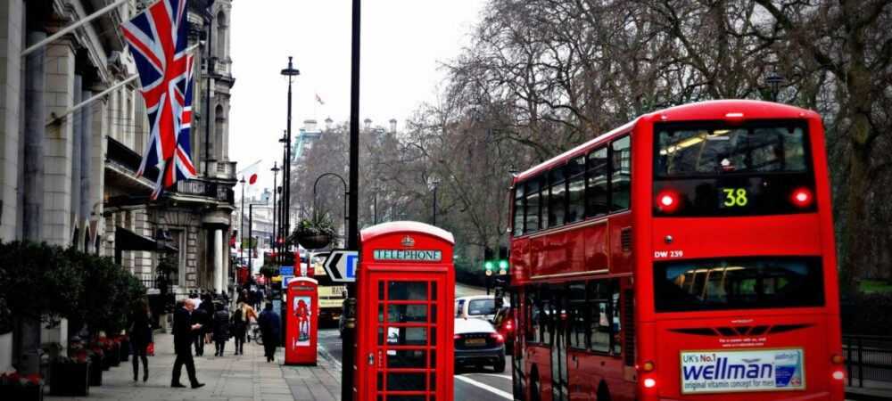 Foto de rua em Londres, com cabine, bandeiras e um ônibus de dois andares