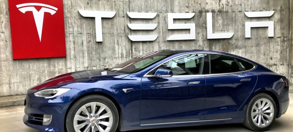 Tesla Model Y diante de um muro com a marca Tesla